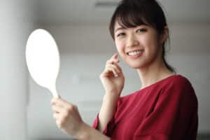 Young woman holding mirror and smiling at her clear skin after IPL photo rejuvenation